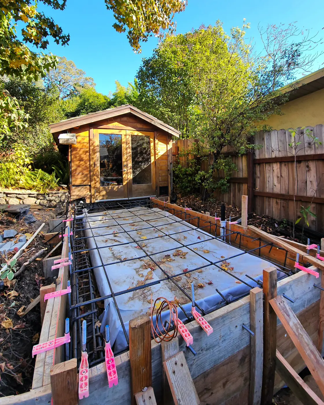 Rebar in wood forms, cedar ADU behind — Backyard ADU Foundation, SF Bay Area