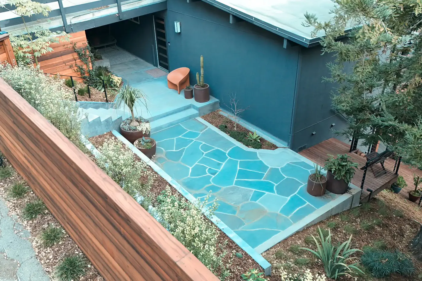 Aerial completed outdoor living: flagstone patio, low retaining walls, deck, mid-century house — Hillside Outdoor Living Transformation, Oakland, CA