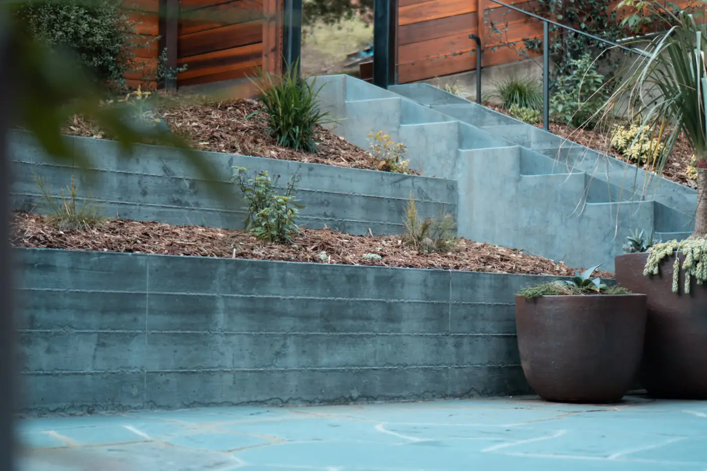 Two-tier concrete retaining wall w/ terraced planters, ceramic pots, flagstone — Hillside Outdoor Living Transformation, Oakland, CA