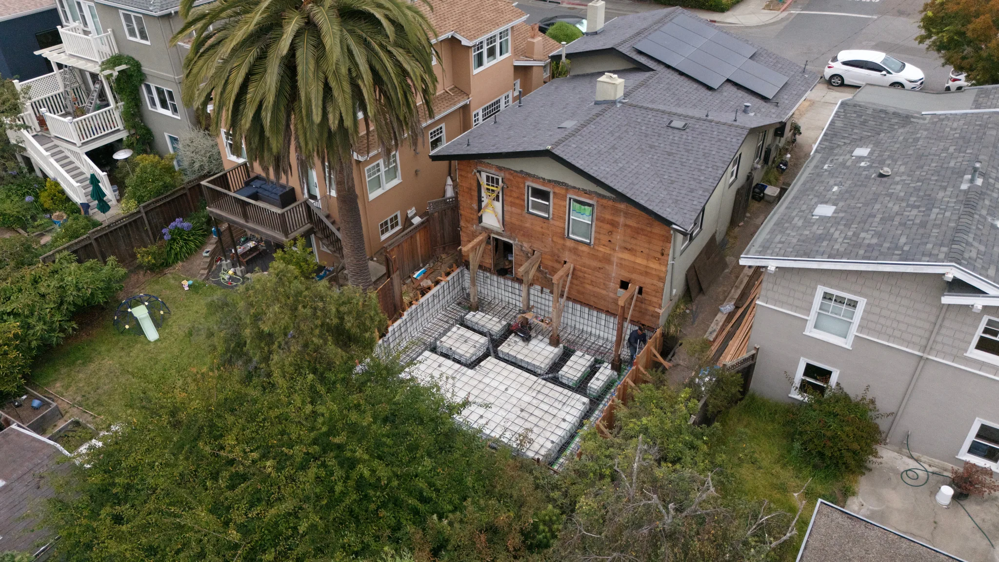 The foundation taking shape behind the opened rear wall, neighbors close on both sides — Albany Home Addition Foundation, Albany, CA