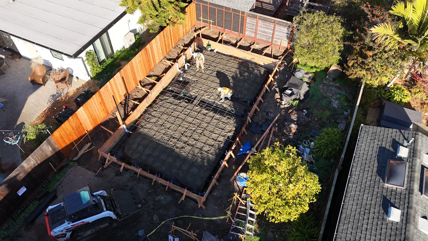 Aerial of the formed footprint and rebar mat with the skid steer staged alongside — Berkeley Backyard Detached ADU, Berkeley, CA
