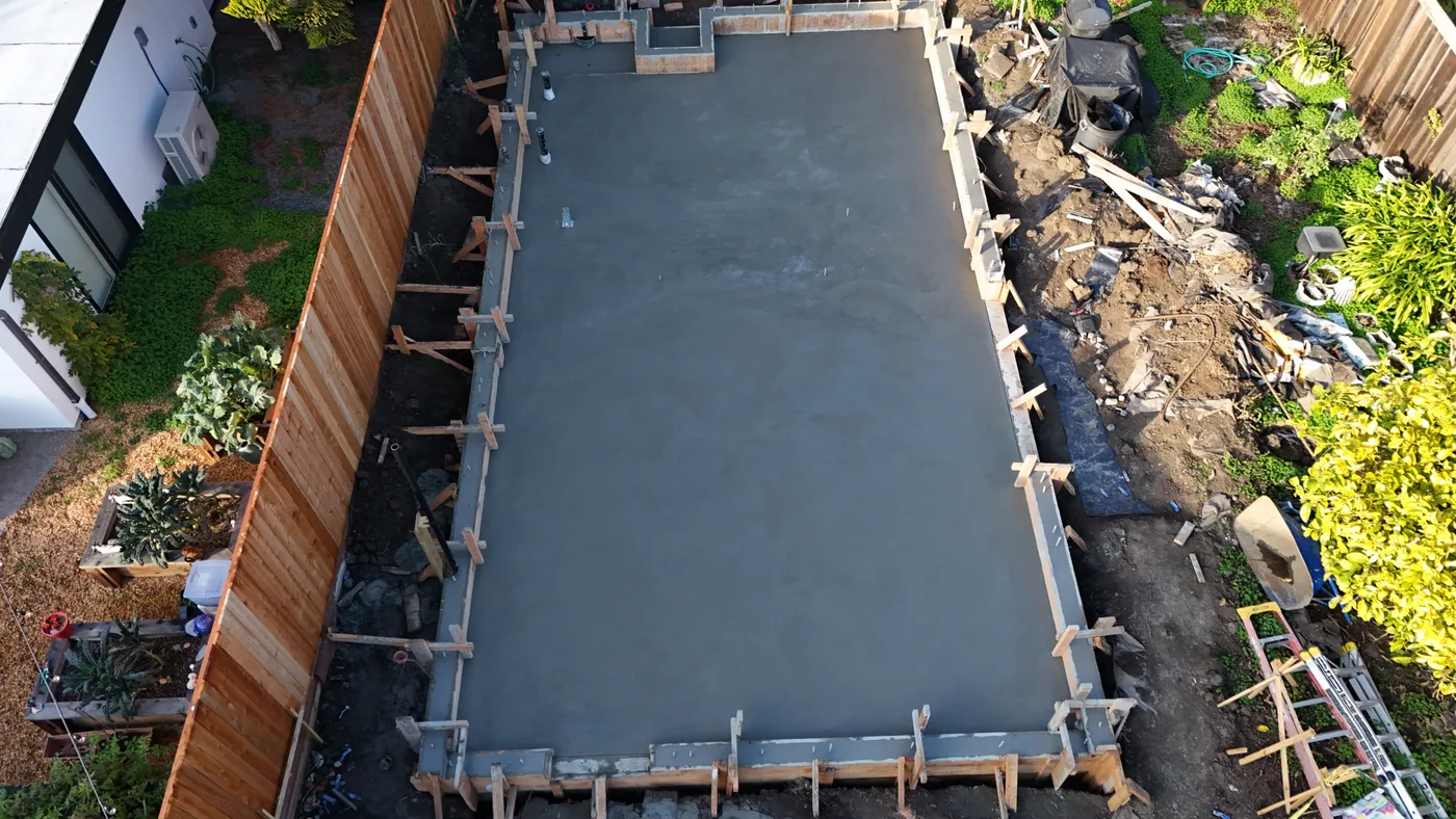 The finished slab running the length of the lot, redwood fence on one side and the staging area on the other — Berkeley Backyard Detached ADU, Berkeley, CA
