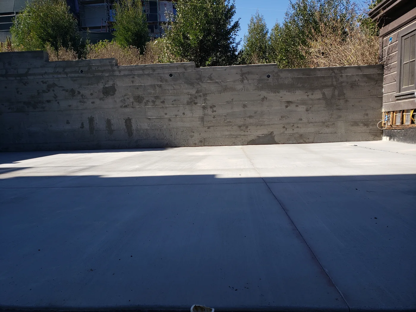 Finished court slab and board-formed retaining wall with weep holes, landscaping above — Lombard Street Basketball Court Foundation, San Francisco, CA