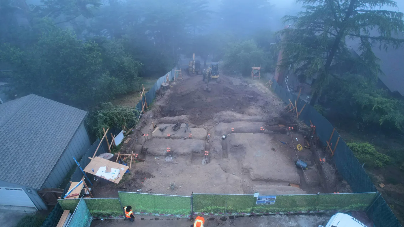Foggy-morning aerial of early excavation with footing trenches, marker stakes, and an excavator — Oakland Hills Custom Home, Oakland, CA