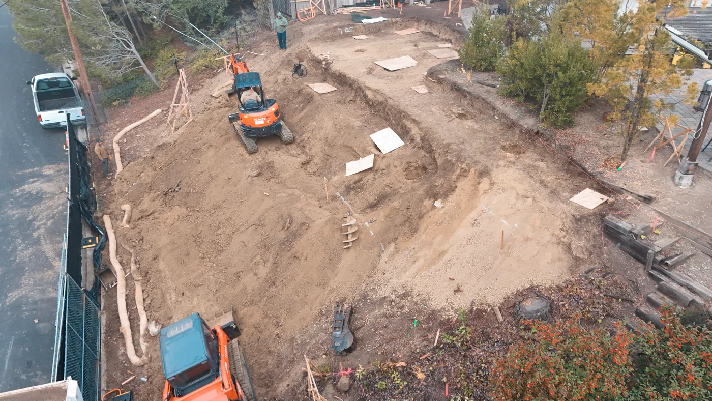 The pad cut into the slope with the excavator working and erosion control run along the street — Steep Hillside Lafayette ADU, Lafayette, CA